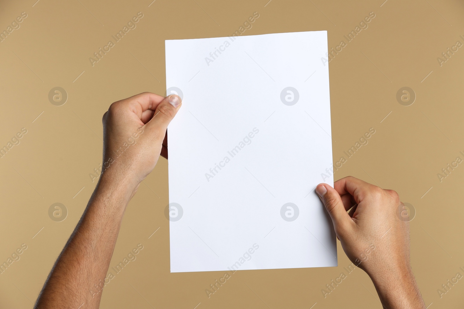 Photo of Man holding sheet of paper on beige background, closeup. Mockup for design