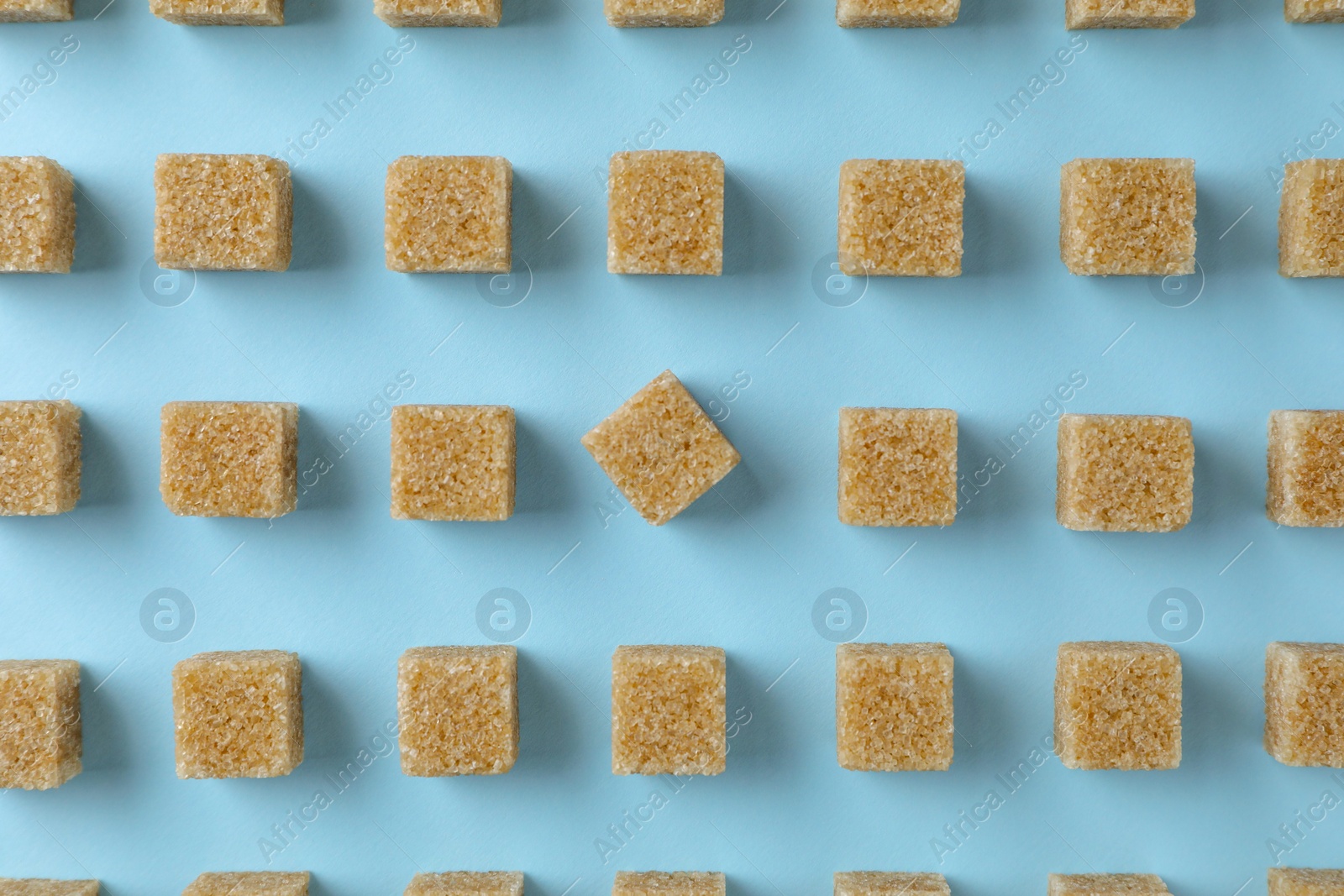 Photo of Brown sugar cubes on light blue background, flat lay