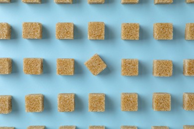 Photo of Brown sugar cubes on light blue background, flat lay