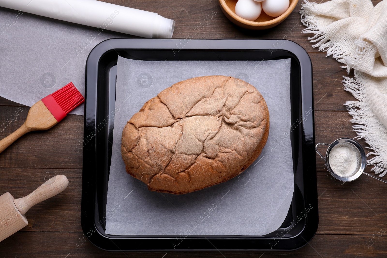 Photo of Baking pan with parchment paper and tasty homemade bread on wooden table, flat lay