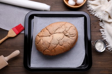 Photo of Baking pan with parchment paper and tasty homemade bread on wooden table, flat lay