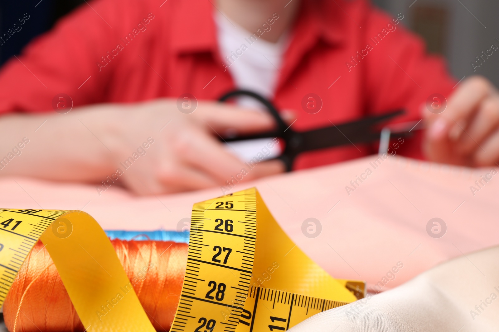 Photo of Woman cutting sewing thread over cloth, focus on measuring tape and spool threads