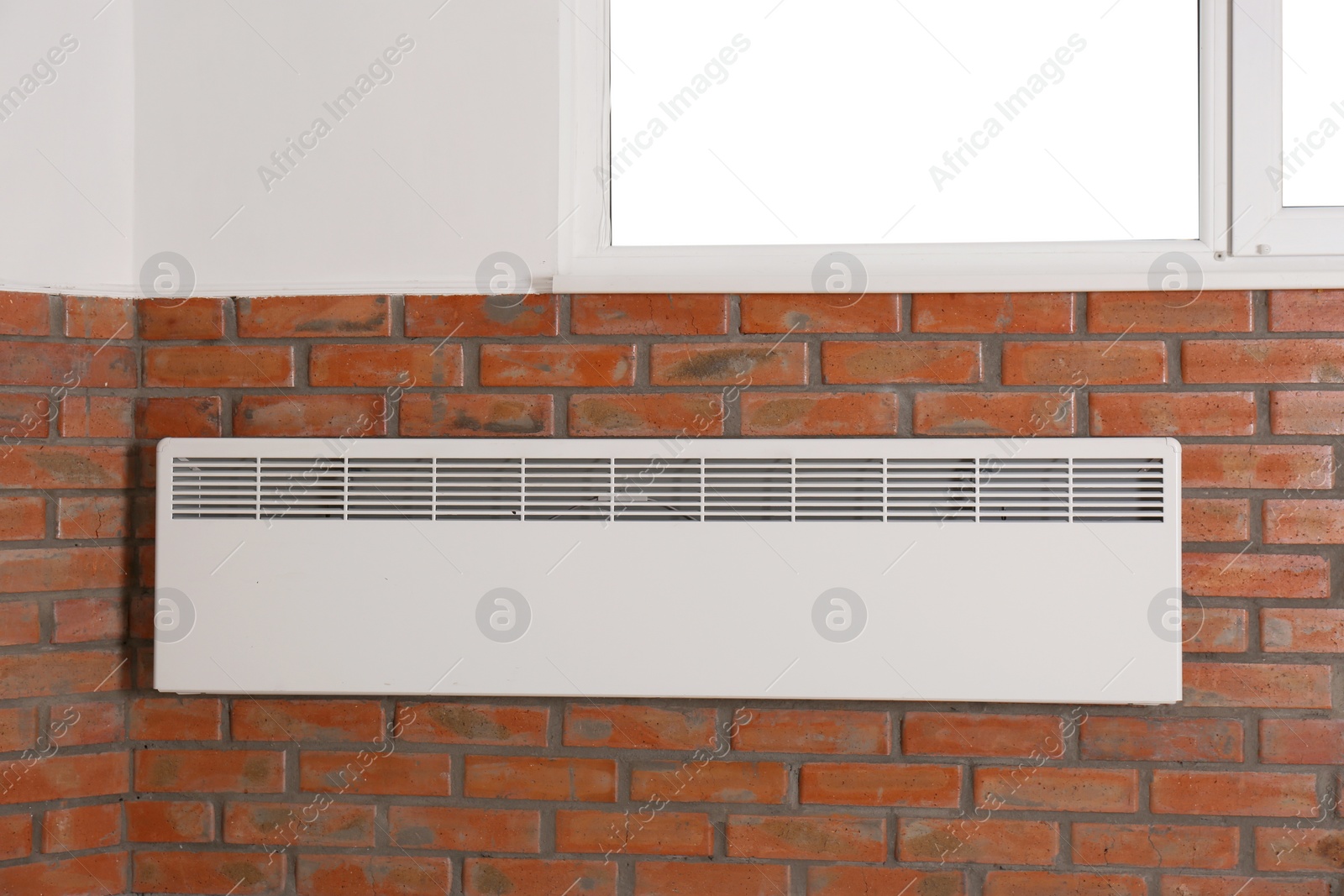 Photo of Heating convector on brick wall under window