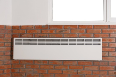 Photo of Heating convector on brick wall under window