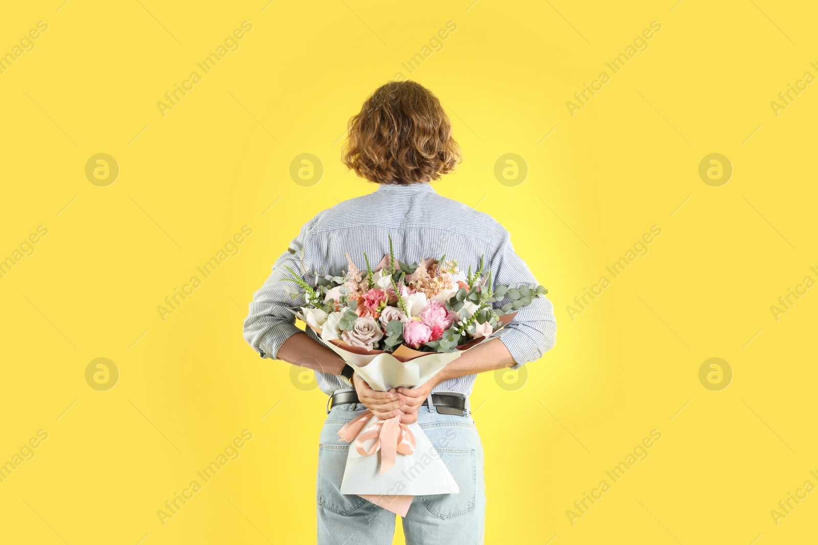 Photo of Man hiding beautiful flower bouquet behind his back on yellow background