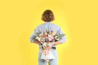 Photo of Man hiding beautiful flower bouquet behind his back on yellow background