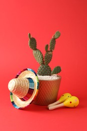 Photo of Mexican sombrero hat, cactus and maracas on red background