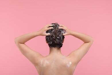 Photo of Woman washing hair on pink background, back view