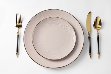 Photo of Stylish golden cutlery and plates on white background, flat lay