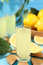 Photo of Tasty limoncello liqueur and lemons on light blue table, closeup