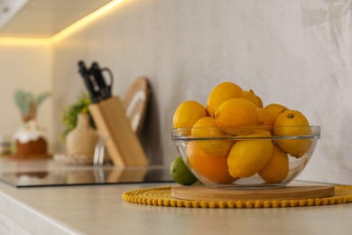 Fresh lemons and orange in glass bowl on white table in kitchen, space for text