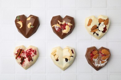 Photo of Tasty chocolate heart shaped candies with nuts on white tiled table, flat lay