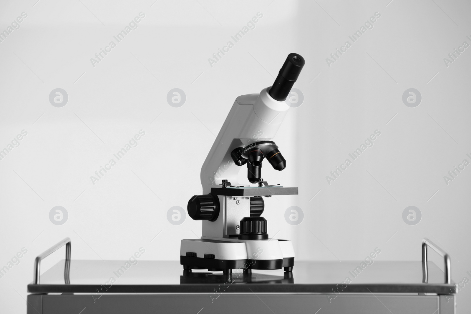 Photo of Modern microscope on metal table against light background