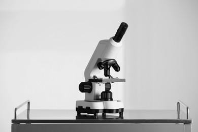 Modern microscope on metal table against light background