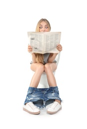 Young woman reading newspaper while sitting on toilet bowl. Isolated on white