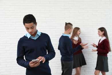 African-American teenager preferring mobile phone to classmates at school. Concept of internet addiction and loneliness