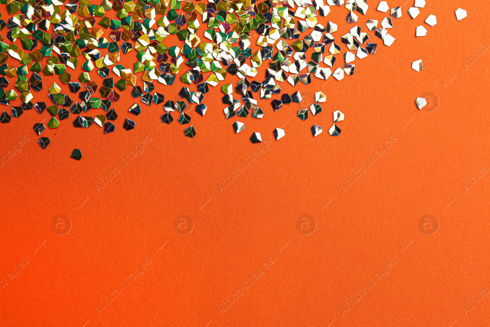 Photo of Shiny bright glitter on coral background, flat lay. Space for text
