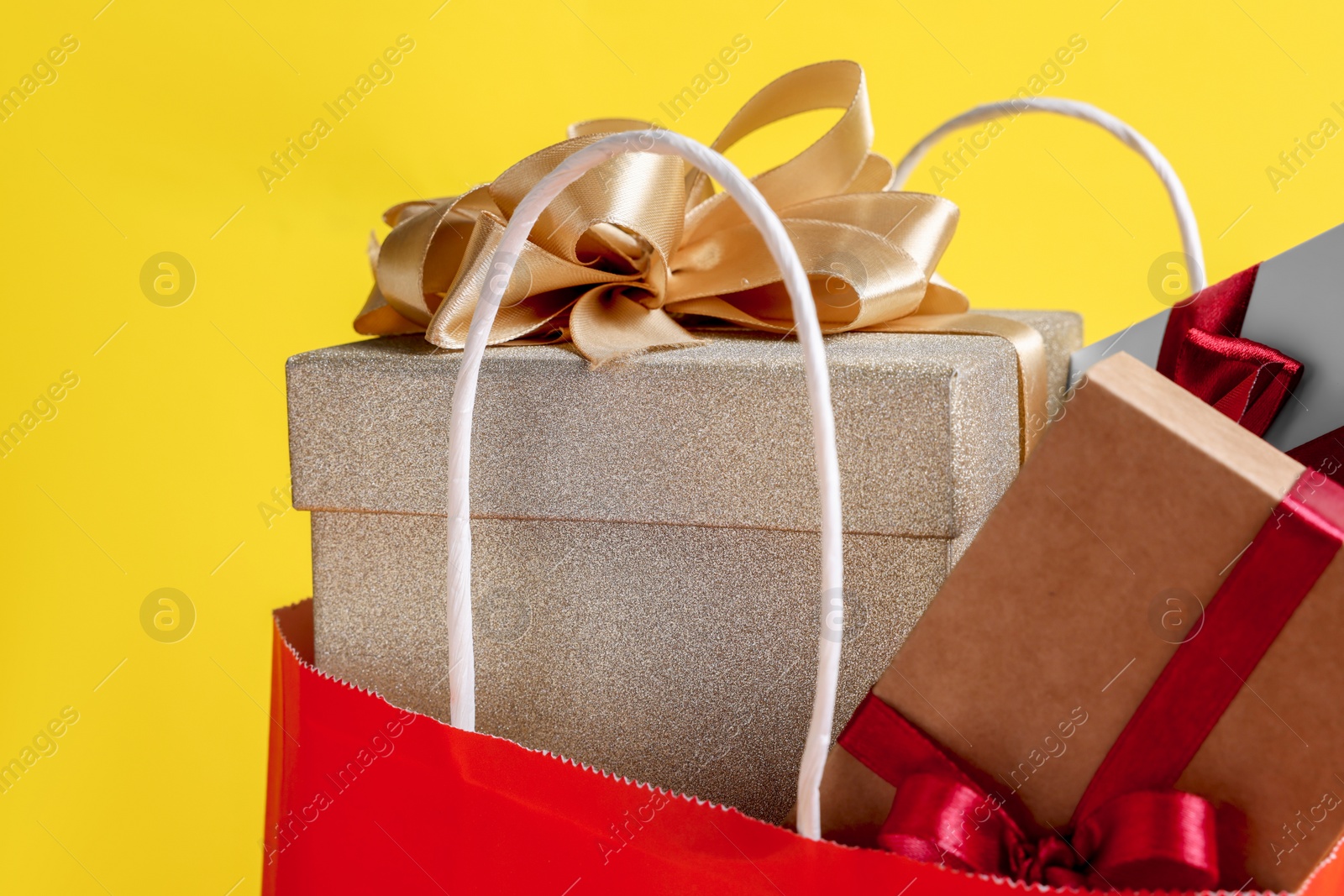 Photo of Red paper shopping bag full of gift boxes on yellow background, closeup