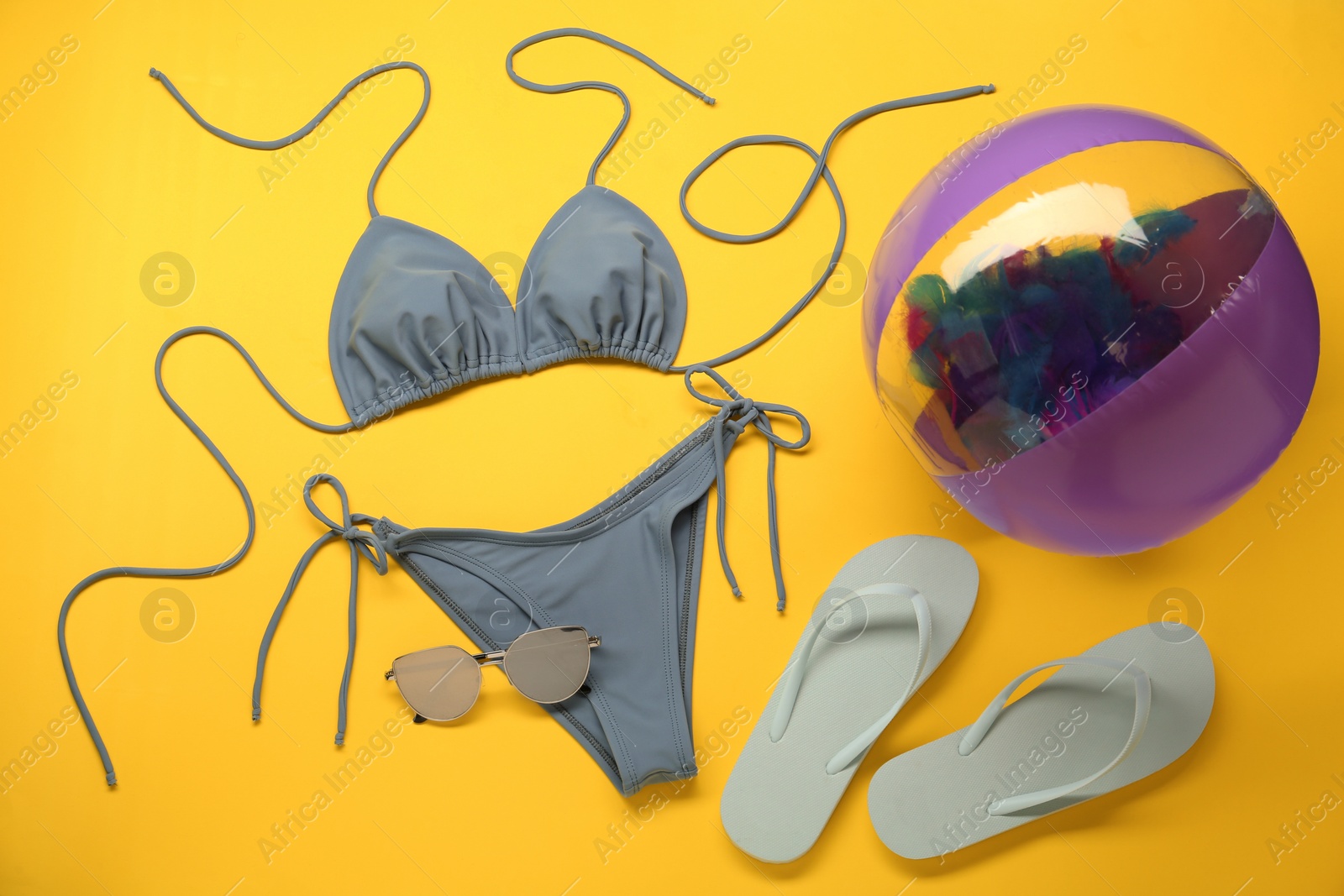 Photo of Stylish blue bikini and beach accessories on yellow background, flat lay