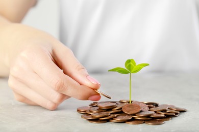 Photo of Woman putting coin onto pile with green sprout at grey table, closeup. Investment concept