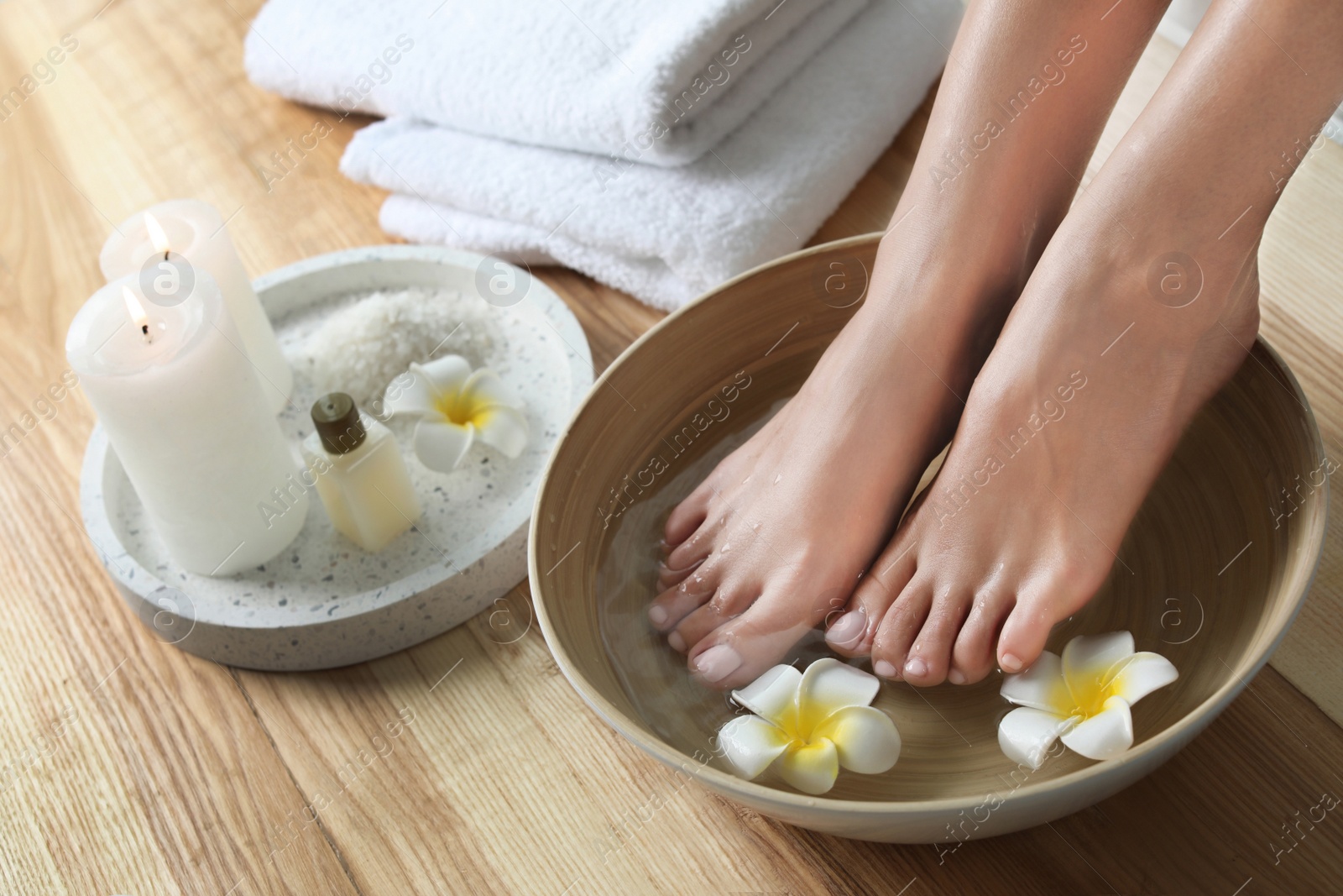 Photo of Closeup view of woman soaking her feet in dish with water and flowers on wooden floor. Spa treatment