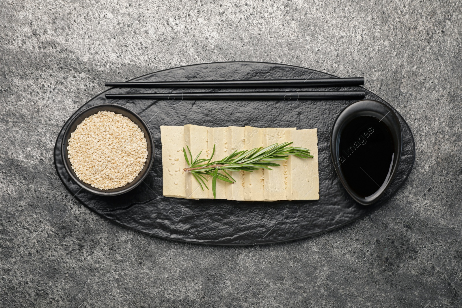 Photo of Delicious tofu with rosemary, soy sauce and sesame seeds on grey table, top view