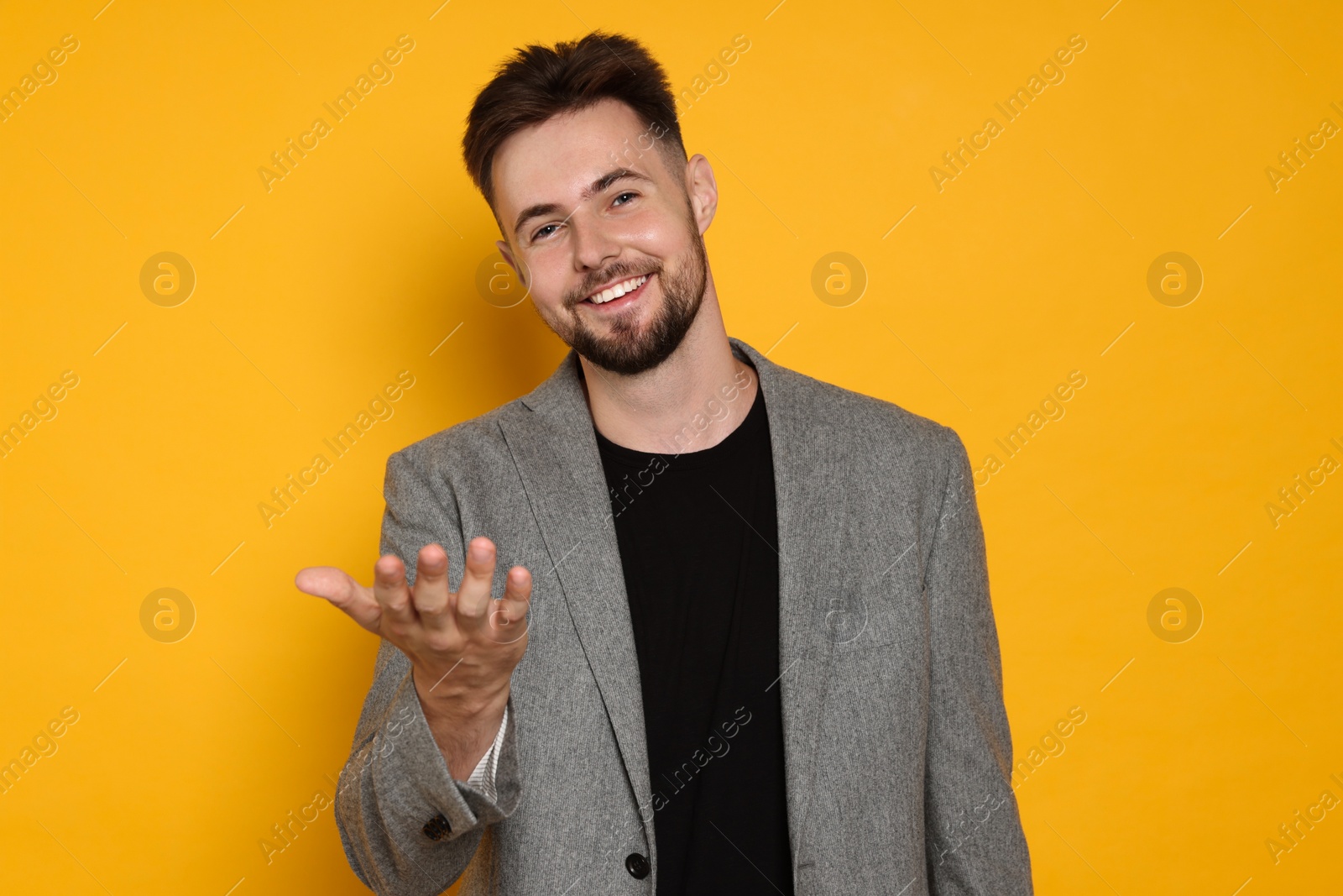 Photo of Handsome man in stylish grey jacket gesturing on yellow background