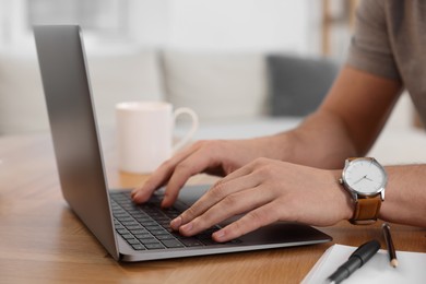 Photo of Man working on laptop at wooden desk indoors, closeup