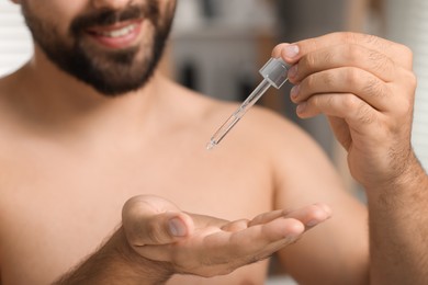 Photo of Young man applying cosmetic serum onto his hand indoors, closeup