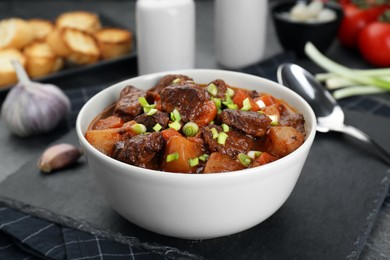 Photo of Delicious beef stew with carrots, green onions and potatoes on grey table, closeup