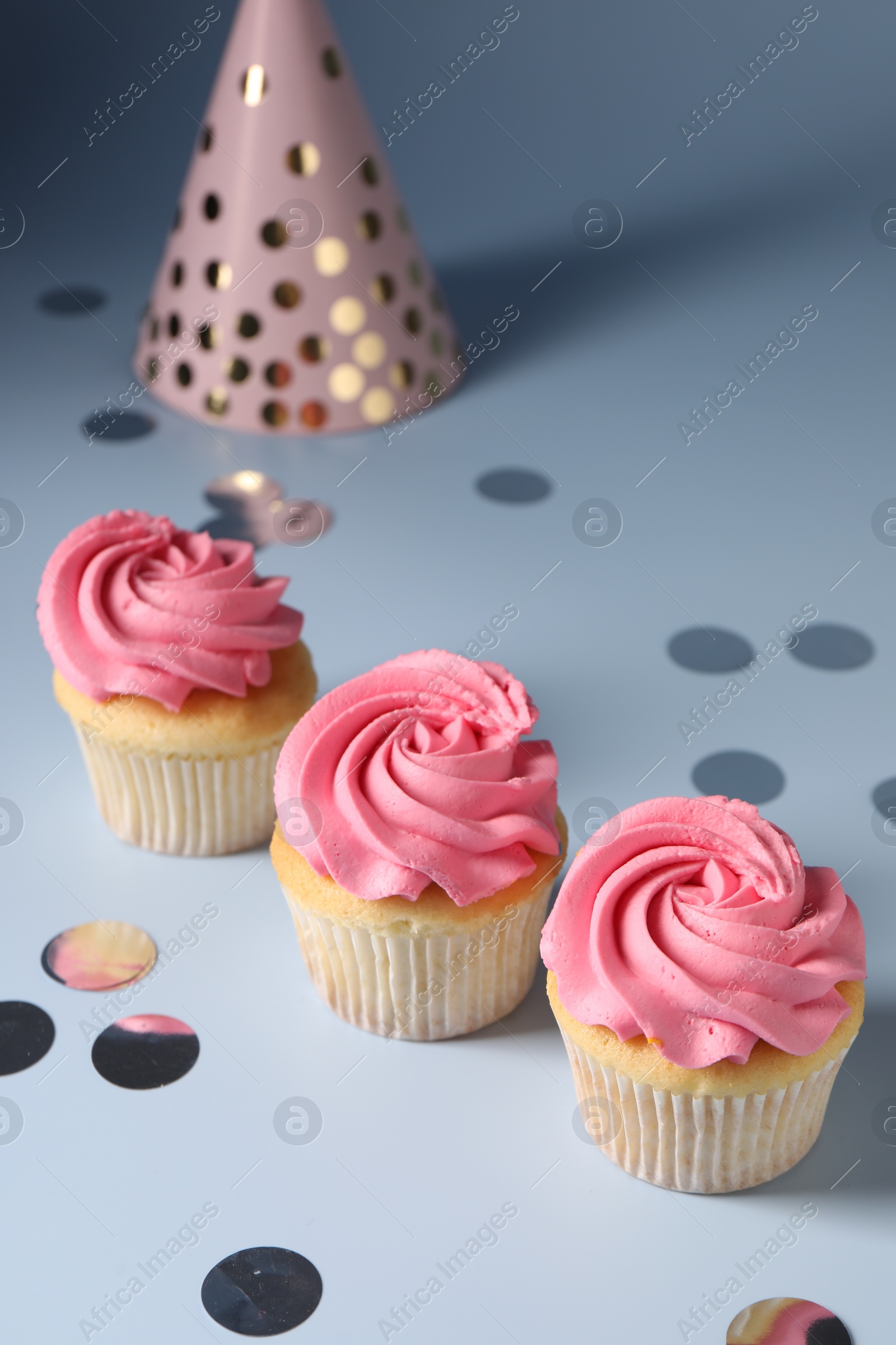 Photo of Delicious cupcakes with bright cream, party hat and confetti on light background, above view