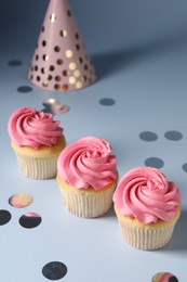 Delicious cupcakes with bright cream, party hat and confetti on light background, above view