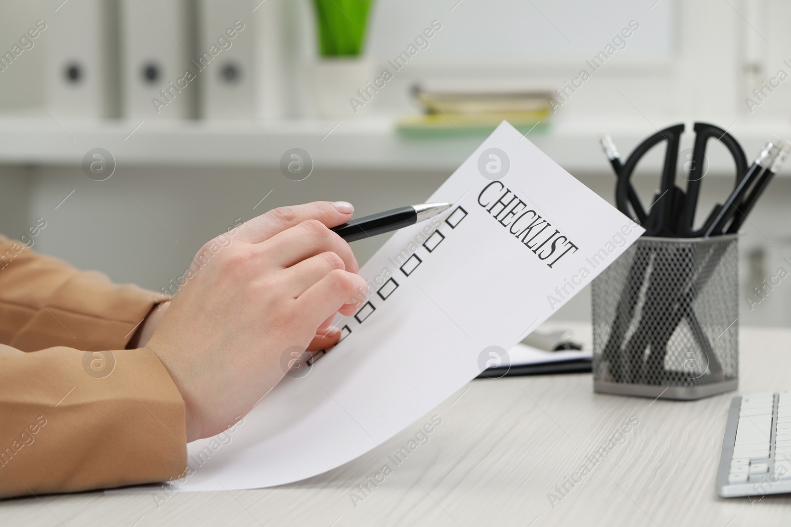Photo of Woman filling Checklist at white wooden table indoors, closeup