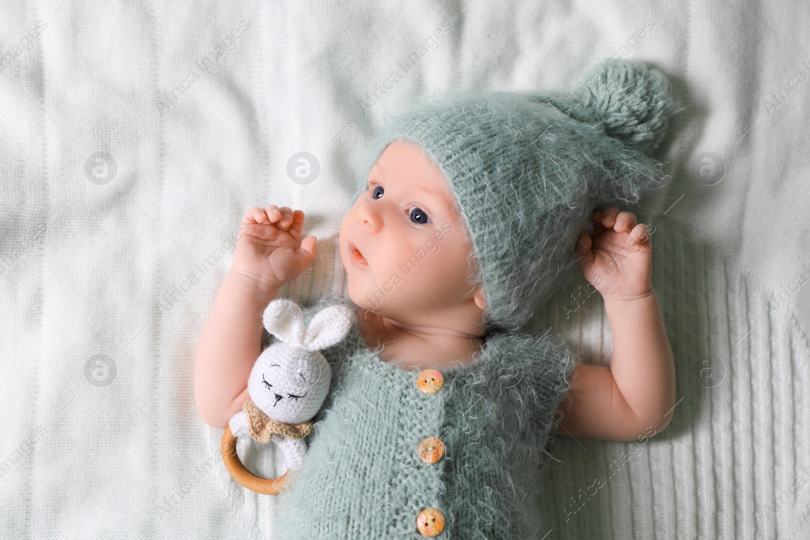 Photo of Cute newborn baby with teething toy on white blanket, top view