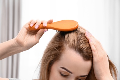 Young woman brushing hair against blurred background, closeup