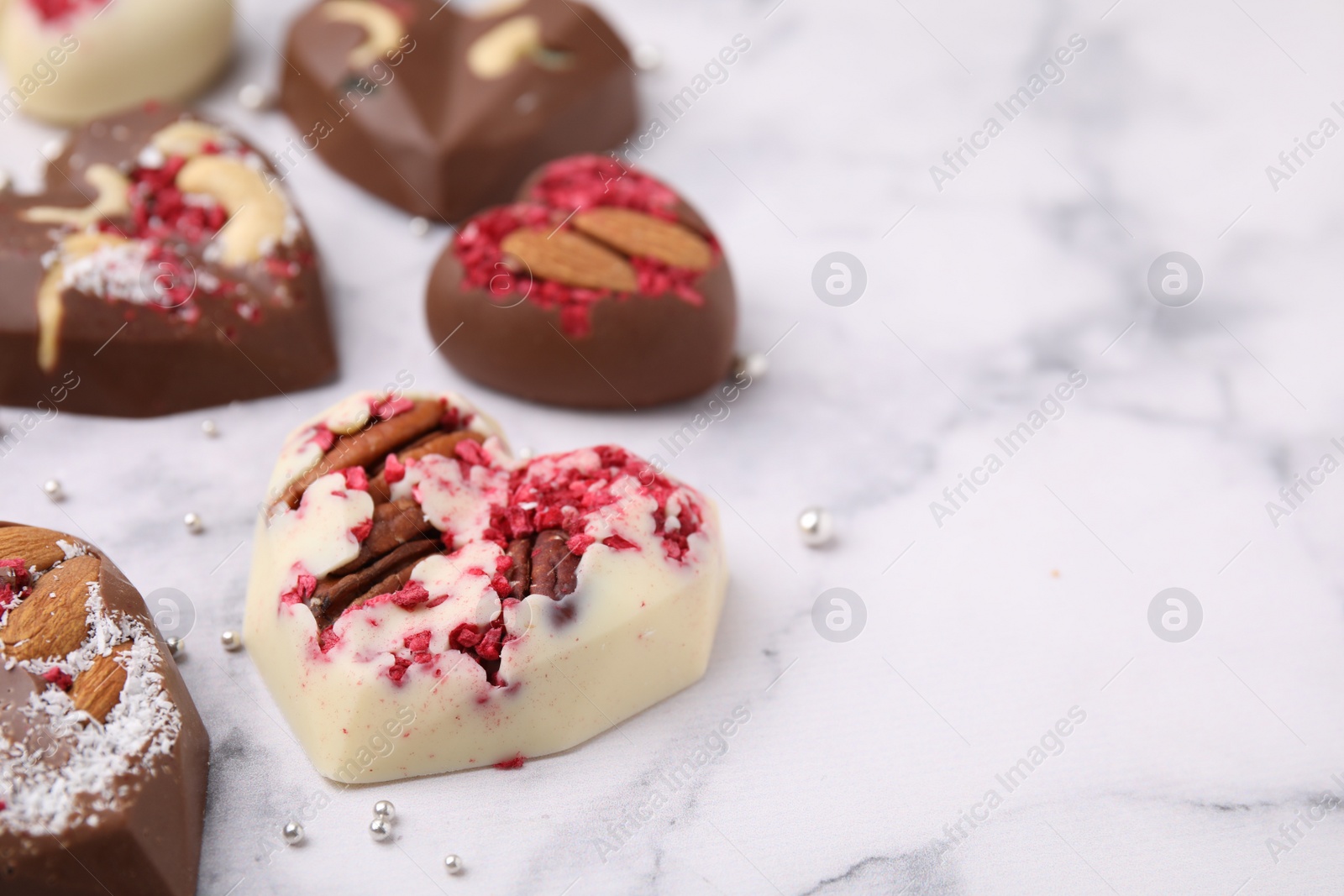 Photo of Tasty chocolate heart shaped candies with nuts on white marble table, closeup. Space for text