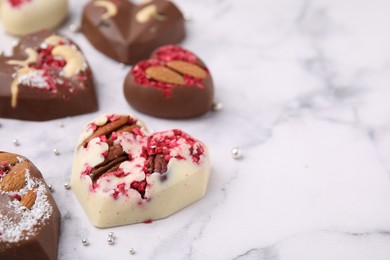 Tasty chocolate heart shaped candies with nuts on white marble table, closeup. Space for text