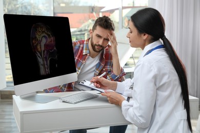 Photo of Young neurologist consulting patient at table in clinic