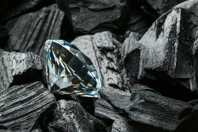 Photo of Beautiful shiny diamond on coals, closeup view