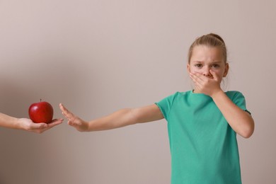 Photo of Cute little girl covering mouth and refusing to eat apple on grey background