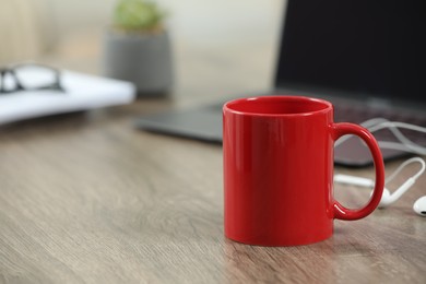 Photo of Red ceramic mug and laptop on wooden table indoors. Space for text