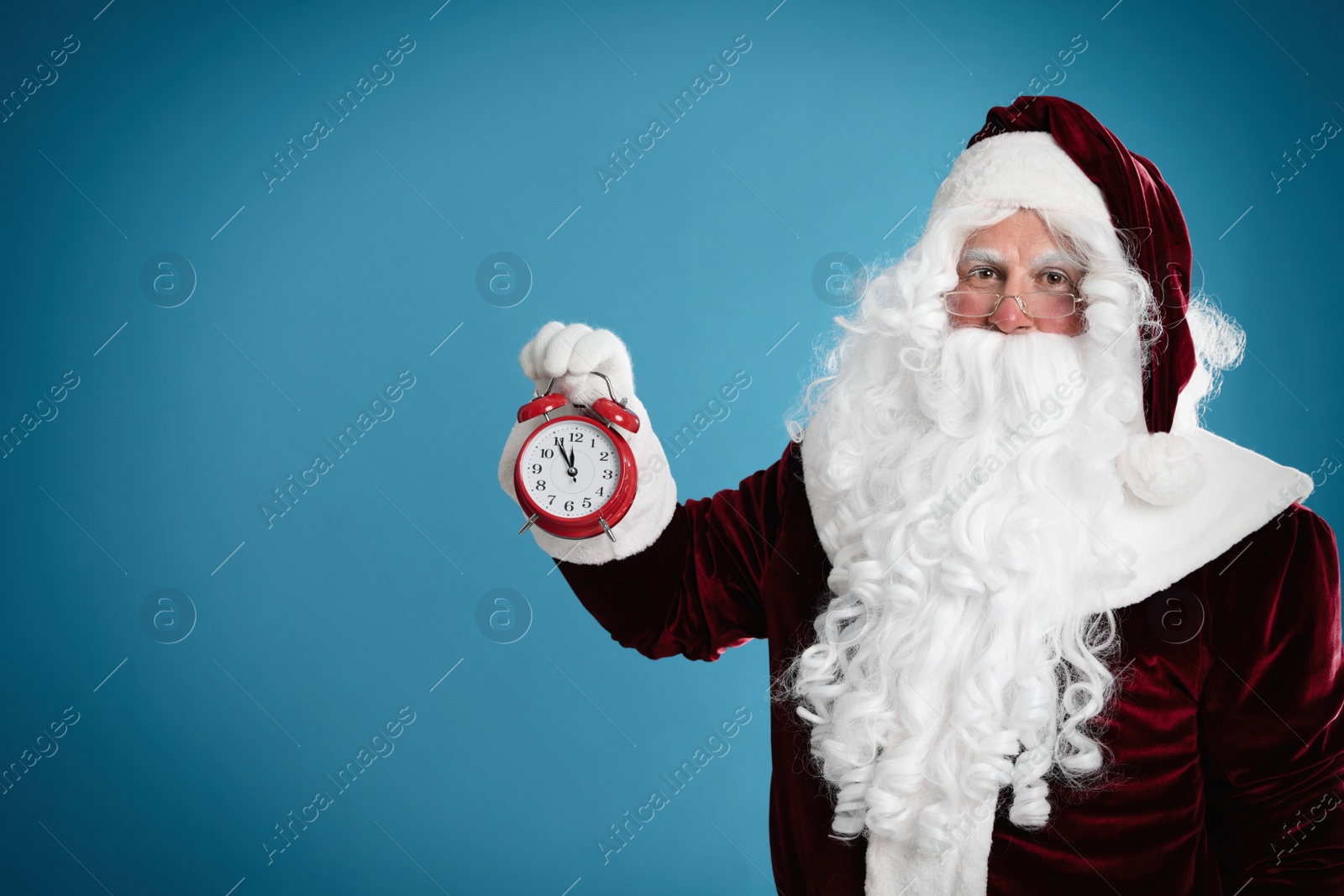 Photo of Santa Claus holding alarm clock on blue background, space for text. Christmas countdown