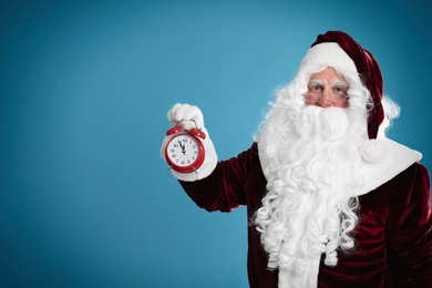 Santa Claus holding alarm clock on blue background, space for text. Christmas countdown