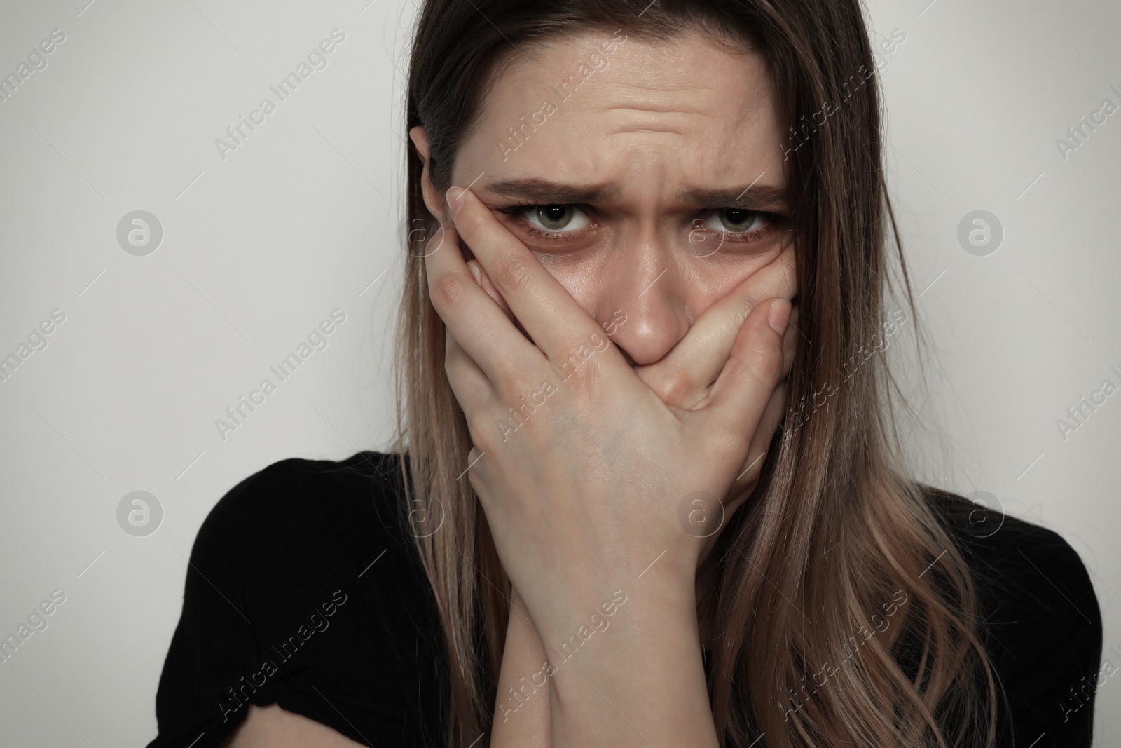 Photo of Scared woman covering mouth with her hands on light background. Stop violence