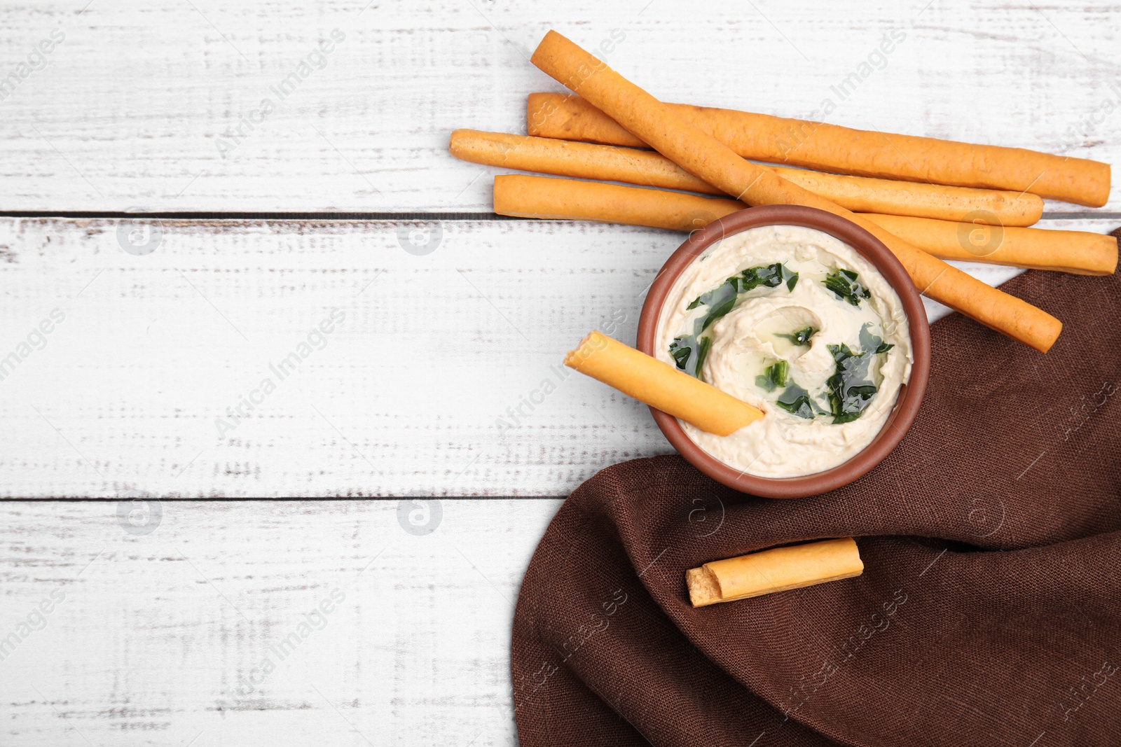 Photo of Delicious hummus with grissini sticks on white wooden table, flat lay. Space for text