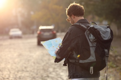 Traveler with world map on city street, back view