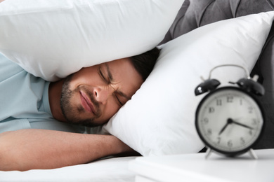 Emotional man covering ears with pillows at home in morning