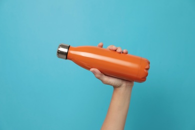 Photo of Woman holding modern orange thermos on light blue background, closeup