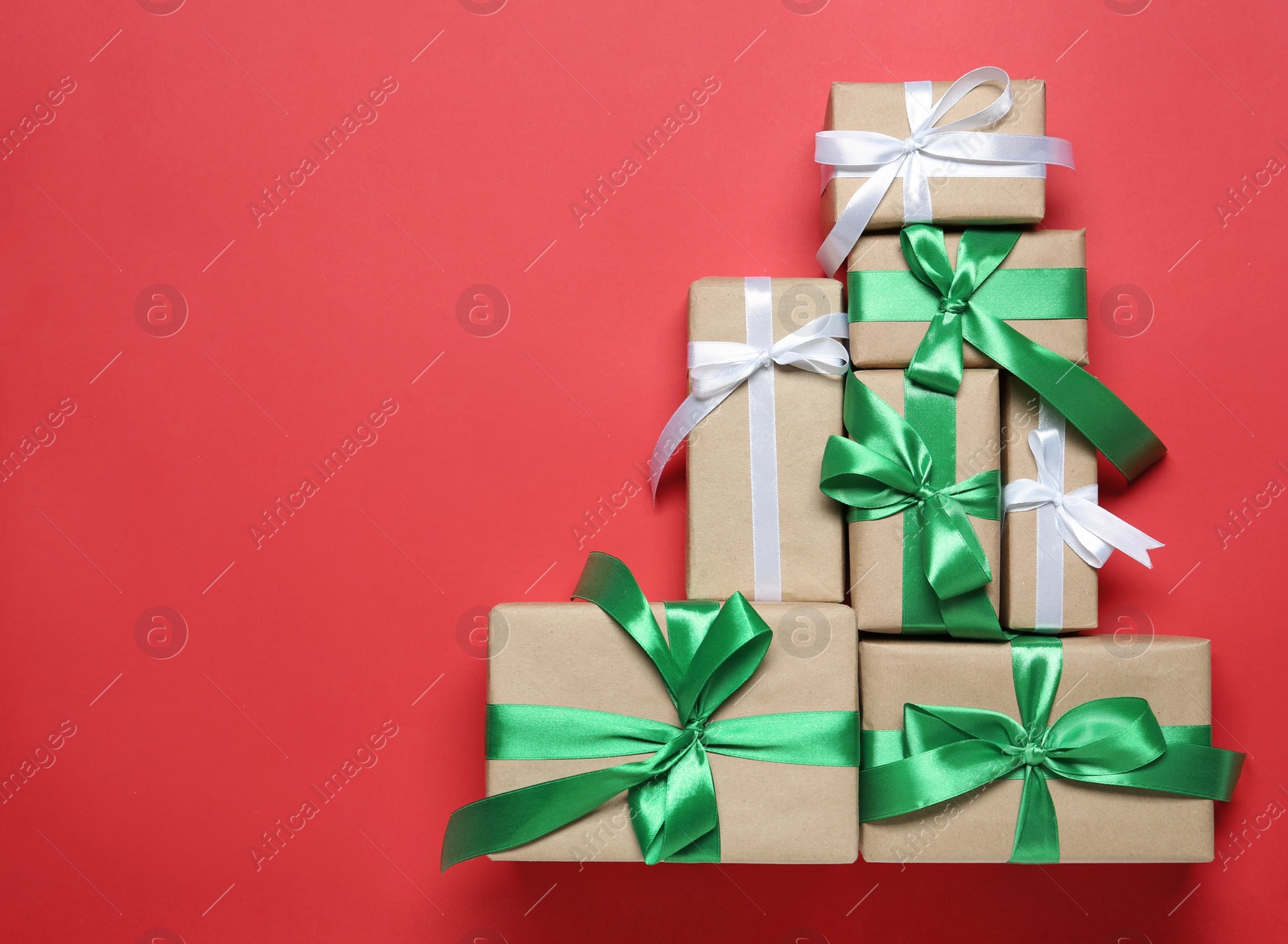 Photo of Christmas tree shape of gift boxes on red background, flat lay. Space for text