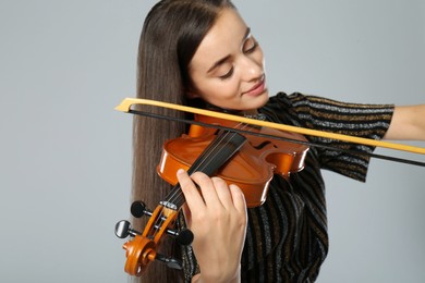 Photo of Beautiful woman playing violin on grey background, closeup